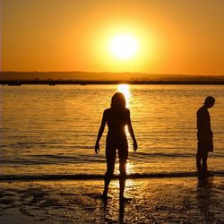 Silhouette of woman standing on beach at sunset