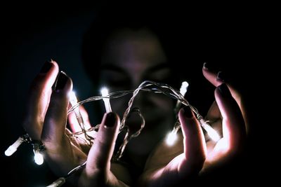 Close-up of woman holding illuminated string lights in darkroom