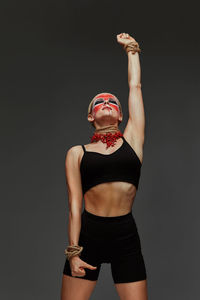 Rear view of woman with arms raised standing against black background