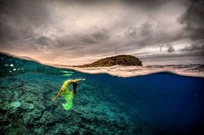 Woman swimming in sea against cloudy sky