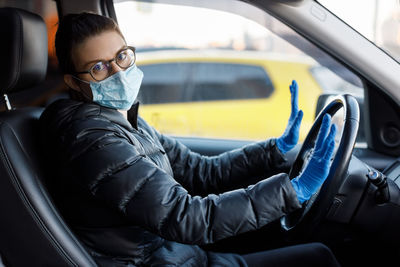 Woman with glasses, medical mask and latex gloves sitting in car and looking at camera. healthcare