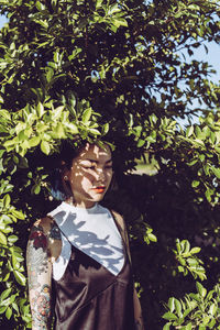 Thoughtful young woman with tattoos standing by plant