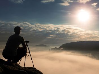 Amateur photographer takes photos with mirror camera on peak of rock. dreamy foggy landscape