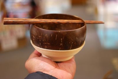 Close-up of hand holding wooden bowl with chopsticks on