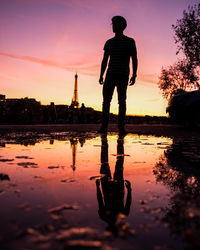 Reflection of silhouette man standing in puddle against sky during sunset