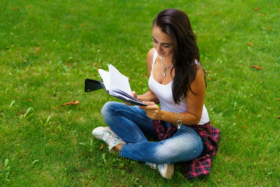 Smiling female student sitting on grass with notepad in hand, preparing