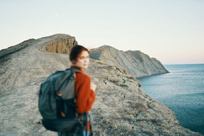 Man standing on rock by sea against clear sky