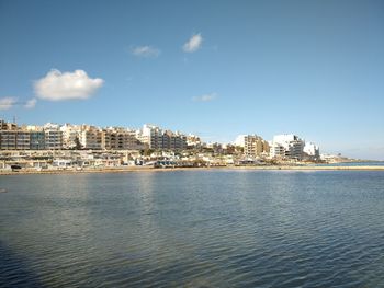 Buildings by sea against blue sky