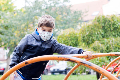 Small kid with kn95 face mask playing alone in the park during coronavirus pandemic.