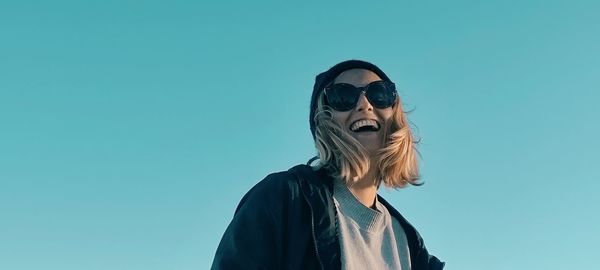 Portrait of young woman wearing sunglasses against clear blue sky