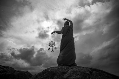 Low angle view of monk holding dream catcher while standing on rock against sky