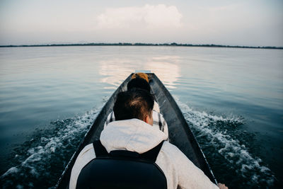 Rear view of man on boat in sea against sky