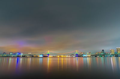 Illuminated city by sea against sky at night