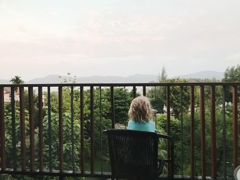 Rear view of woman sitting on railing against sky