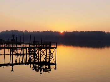 Silhouette pier on lake against sky during sunrise