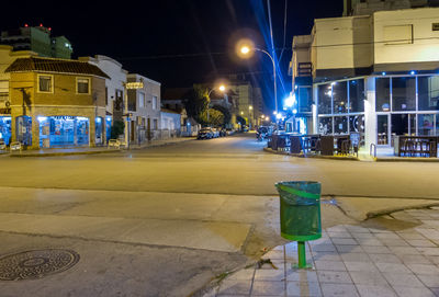 Illuminated street light on road by building at night