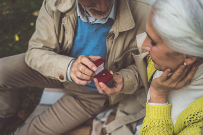 Midsection of couple holding mobile phone while sitting outdoors