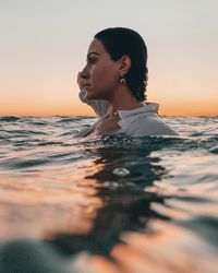 Woman looking away while swimming in sea against sky during sunset