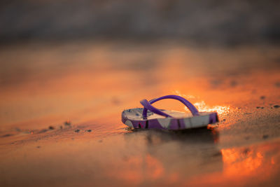 Close-up of flip-flop at shore during sunset