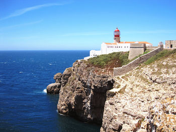 Lighthouse on building by sea against blue sky
