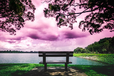 Bench by lake against sky