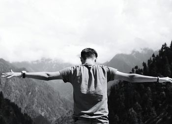 Rear view of man with arms outstretched standing against mountains