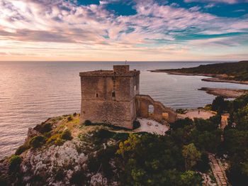 Old building by sea against sky during sunset