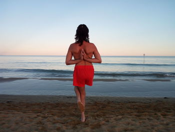 Rear view of shirtless man practicing yoga against sea during sunset