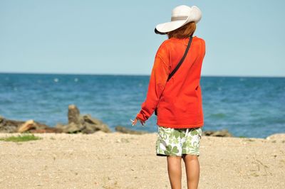 Rear view of woman standing at beach against clear sky