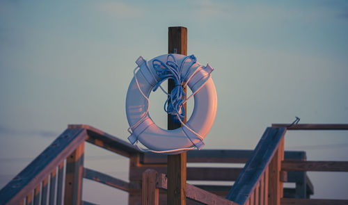 Low angle view of wooden post against sky holding life preserver