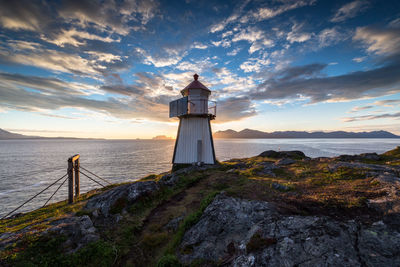 Lighthouse on rock formation by sea against sky during sunset