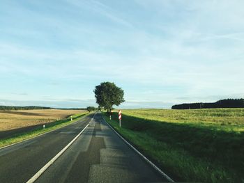 Road passing through field against cloudy sky