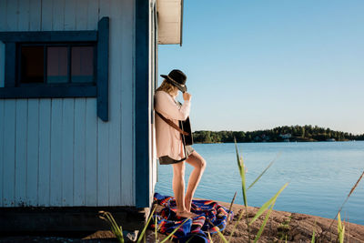 Woman stood against a beach hut playing the guitar alone in the sun