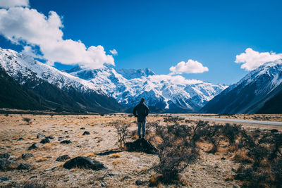 Rear view of man standing on snowcapped mountain against sky