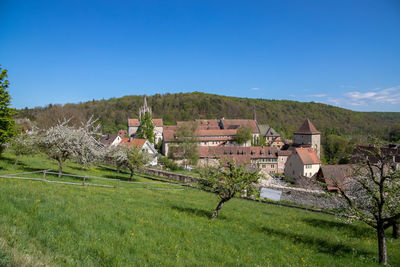 Houses on field by buildings against blue sky