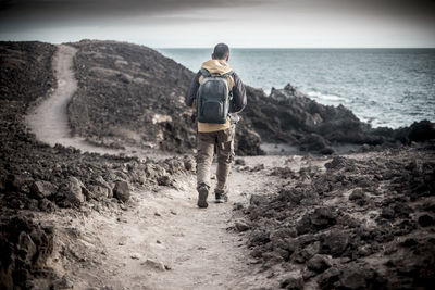 Rear view of man with backpack walking towards sea 