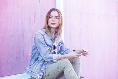 Portrait of young woman using mobile phone against wall