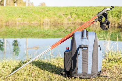 Backpack with hiking poles at lakeshore during sunny day