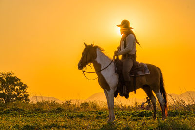 Man riding horse on field during sunset