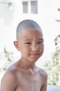 Summer shoulder portrait of a tanned asian boy with a bald haircut, looking at camera