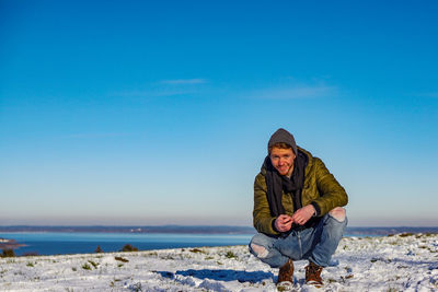 Portrait of man crouching against sea during winter