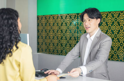 At the airport check-in counter, a passenger hands over his documents to the manager via a counter 