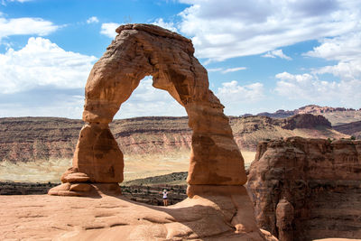 Woman standing at rock formation against cloudy sky