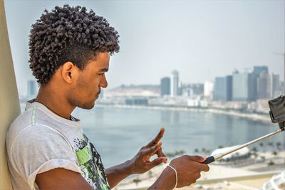 Young man showing peace sign while taking selfie with sea in background