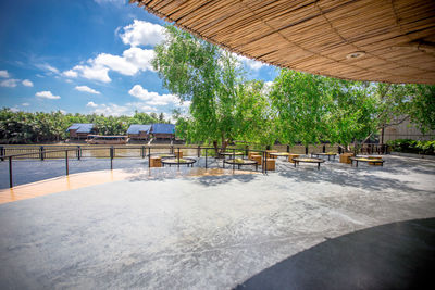 Empty chairs and tables by swimming pool against sky