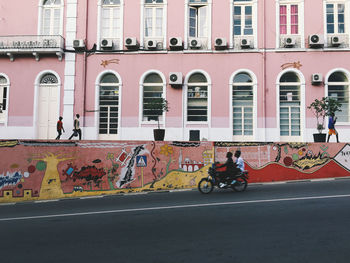Road by graffiti on wall against pink building in city