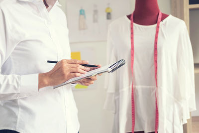 Midsection of female fashion designer writing on book in office