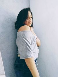 Side view of young woman standing against wall