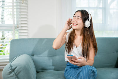 Young woman using phone while sitting on sofa at home