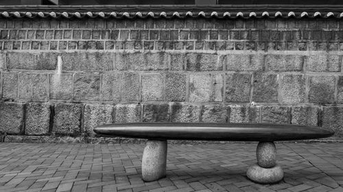 Empty bench on footpath against wall